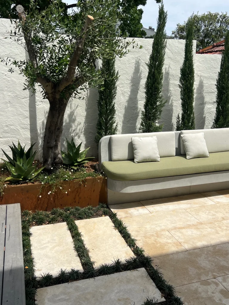 Olive-cushioned courtyard seating beside a tree and rust-toned garden edging
