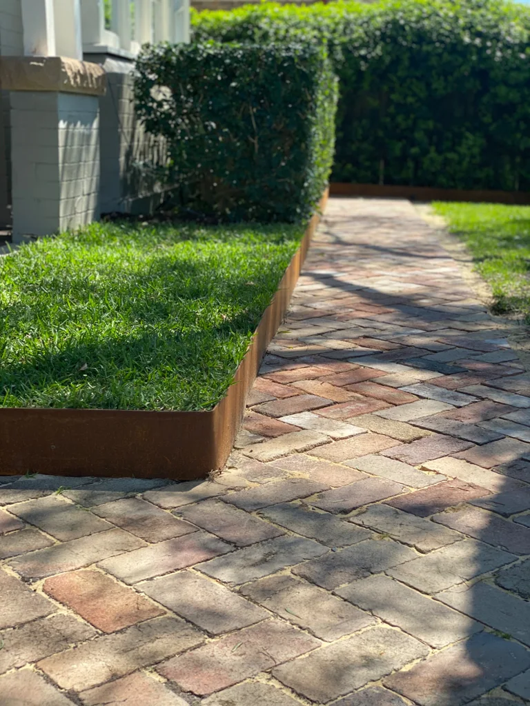 Brick path beside lawn and a rust-toned garden edge