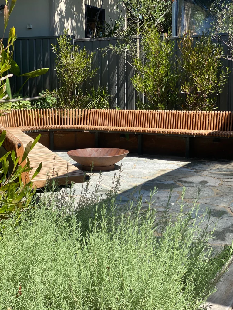 Curved timber seating and a fire bowl beside planted borders