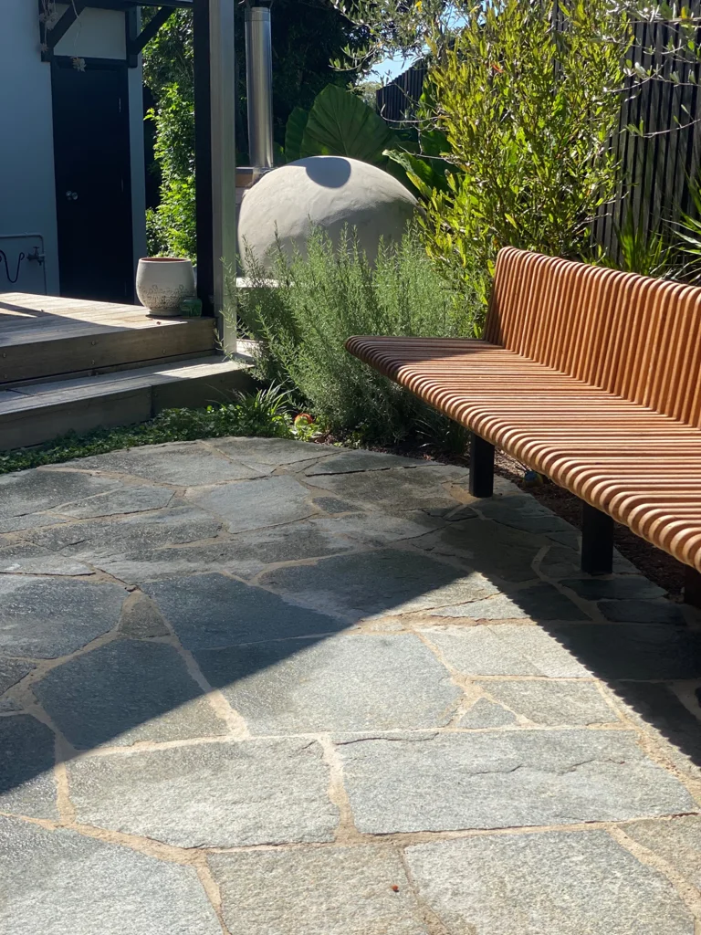 Curved timber garden bench beside stone paving